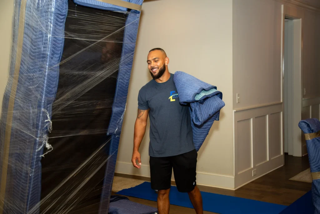 Professional mover transporting a couch wrapped in protective packing material.
