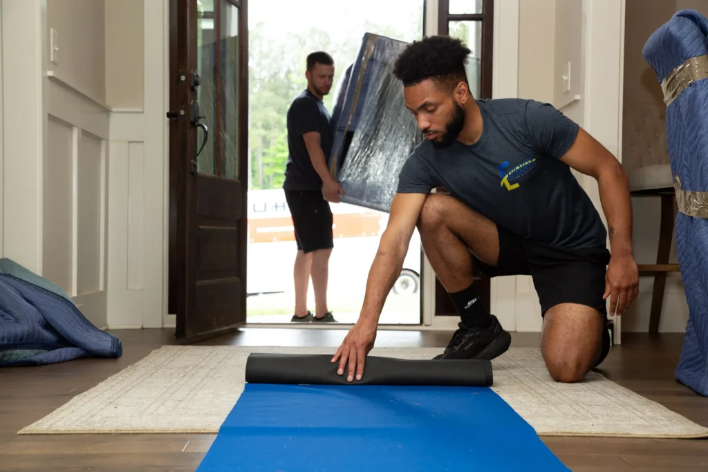 Professional mover placing protective floor padding along a walkway during a residential move.