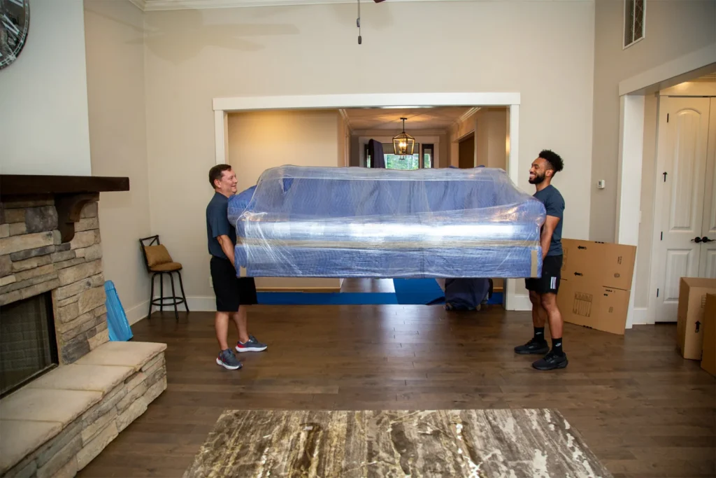 Two professional movers carefully carrying a couch wrapped in protective padded blankets. during a move