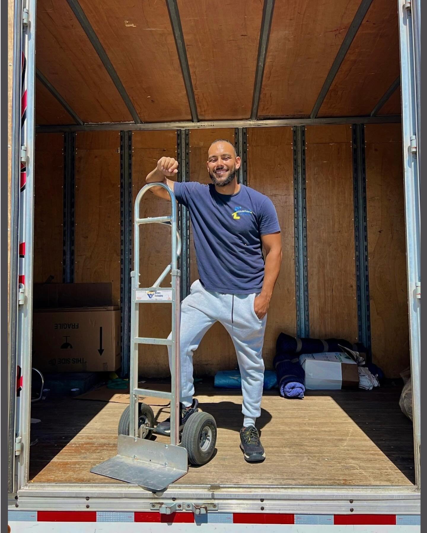 Friendly mover posing with a hand truck inside a moving van ready for loading and transport.