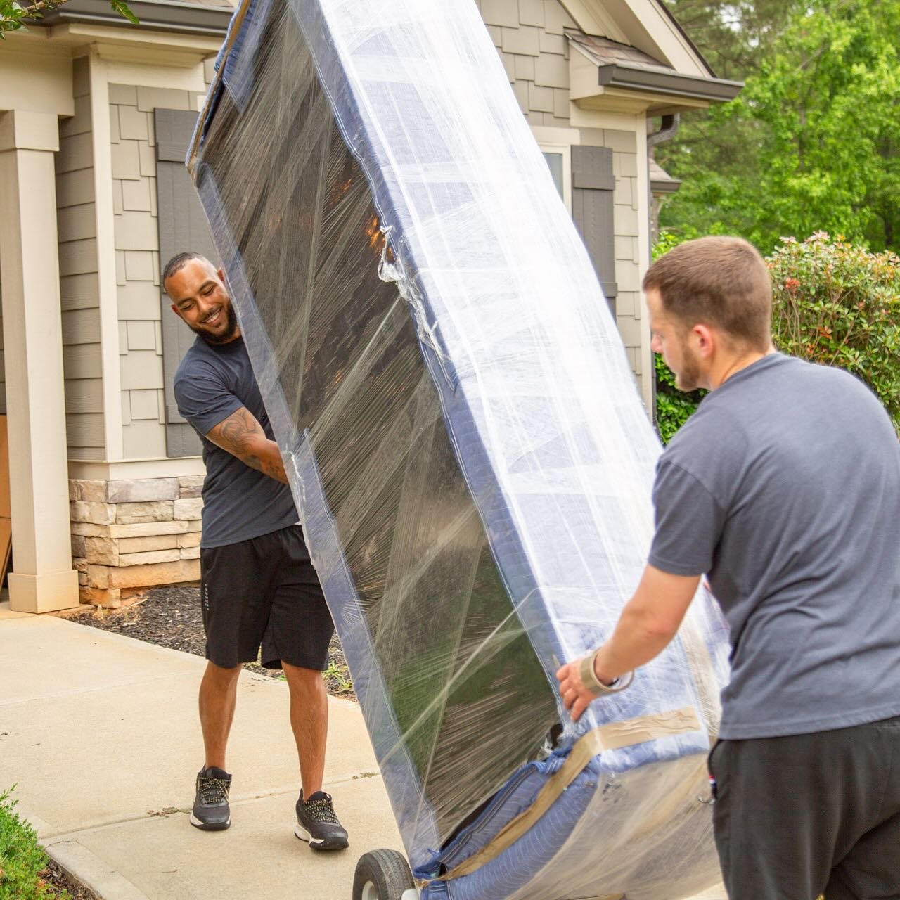 Professional movers lifting a large, wrapped piece of furniture during a move.
